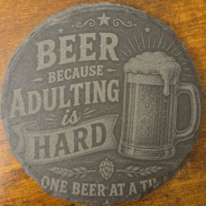 Round black slate coaster engraved with Beer Because Adulting Is Hard and a beer mug